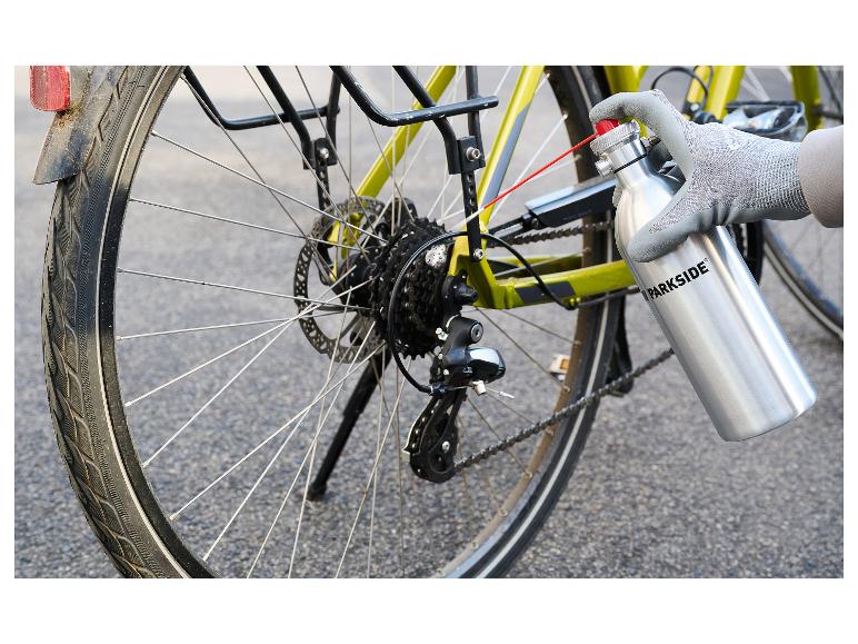 Hand im Handschuh schmiert eine Fahrradkette mit einer Sprühflasche.