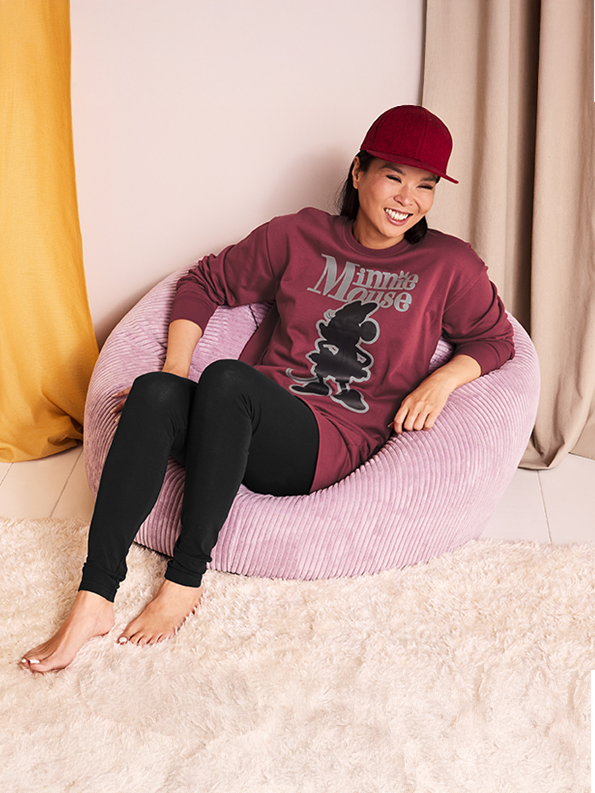 Frau in Minnie-Maus-Schlafanzug und Mütze sitzt in einem rosa Sitzsack.