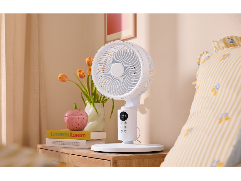 Weißer Tischventilator auf einem hölzernen Nachttisch neben dem Bett.