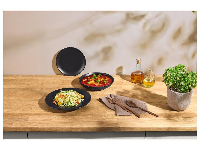 Teller mit Pasta und Suppe in schwarzen Schalen, mit Kupferbesteck und Öl auf einem Holztisch.