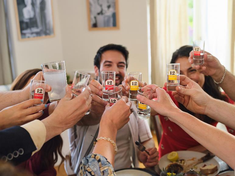Freunde stoßen mit Ouzo-Gläsern am Esstisch an.