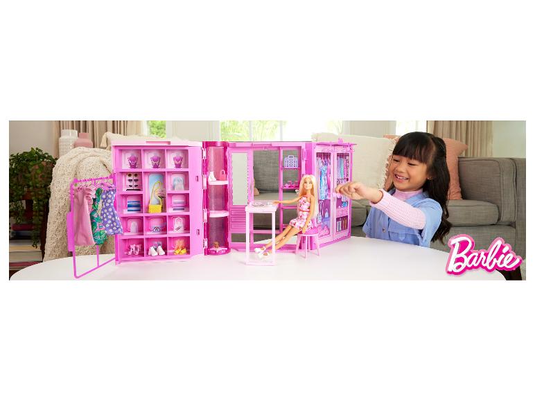 Mädchen spielt mit einem pinken Puppenschrank, Puppe und Accessoires auf einem weißen Tisch.