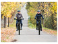Zwei Personen fahren mit E-Bikes durch einen Wald im Herbst.