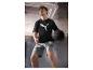 Mann in schwarzem T-Shirt und grauen Shorts hält einen Medizinball im Fitnessstudio.