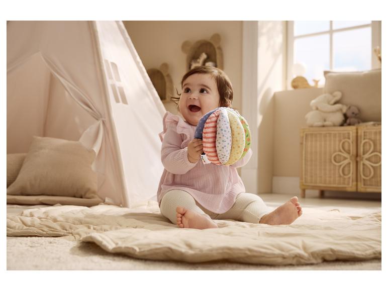 Baby im rosa LUPILU® Musselin-Set spielt auf einer Spielmatte.