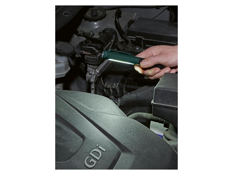 Mann beleuchtet Automotor mit Taschenlampe, GDi-Schriftzug sichtbar.