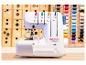 Weiße Overlock-Nähmaschine mit bunten Fäden, vor einem Hintergrund aus Holzschubladen.