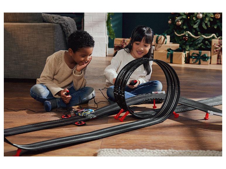 Zwei Kinder spielen mit einer Carrera Rennbahn mit einem Polizeiauto.