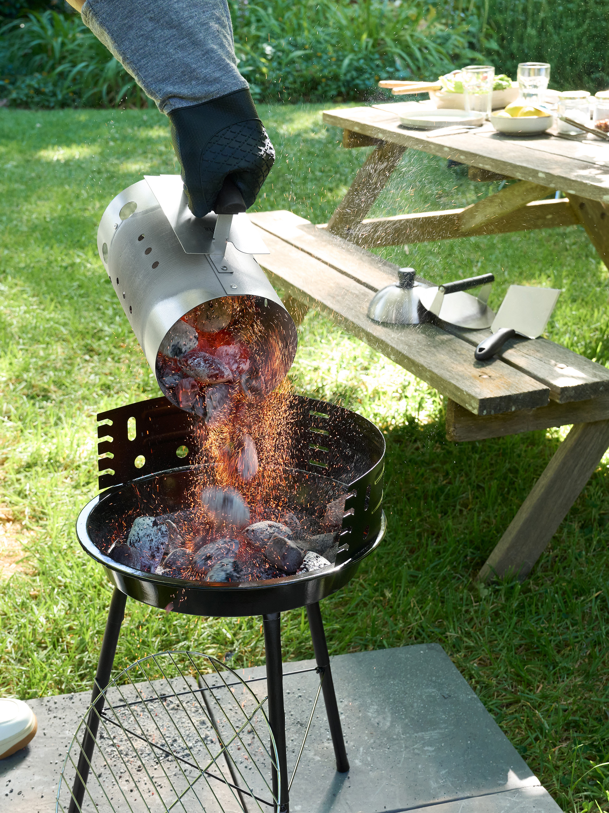 Glühende Kohlen werden aus einem Anzündkamin in einen Holzkohlegrill im Garten geschüttet.