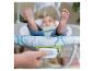 Nahaufnahme einer Hand, die einen Knopf an einer Babywippe drückt, mit Baby im Hintergrund.