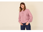 Frau in rosa Strickjacke mit Knöpfen und dunkelblauer Jeans, Hände in den Taschen.