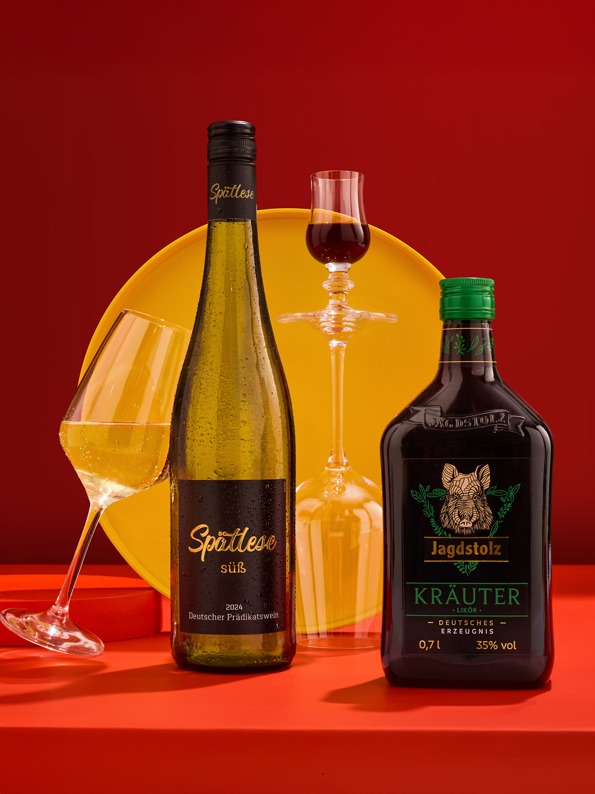 Flasche Weißwein und Flasche Kräuterlikör mit Gläsern auf rotem und gelbem Hintergrund.
