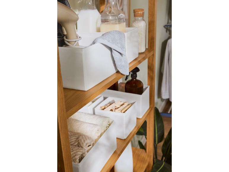 Holzregal mit weißen Aufbewahrungsboxen, Föhn, Handtüchern und Flaschen.