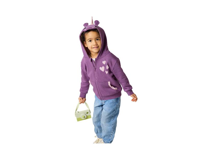 Kleinkind in lila Einhorn-Kapuzenpullover und Jeans, hält eine Spielzeugkamera.