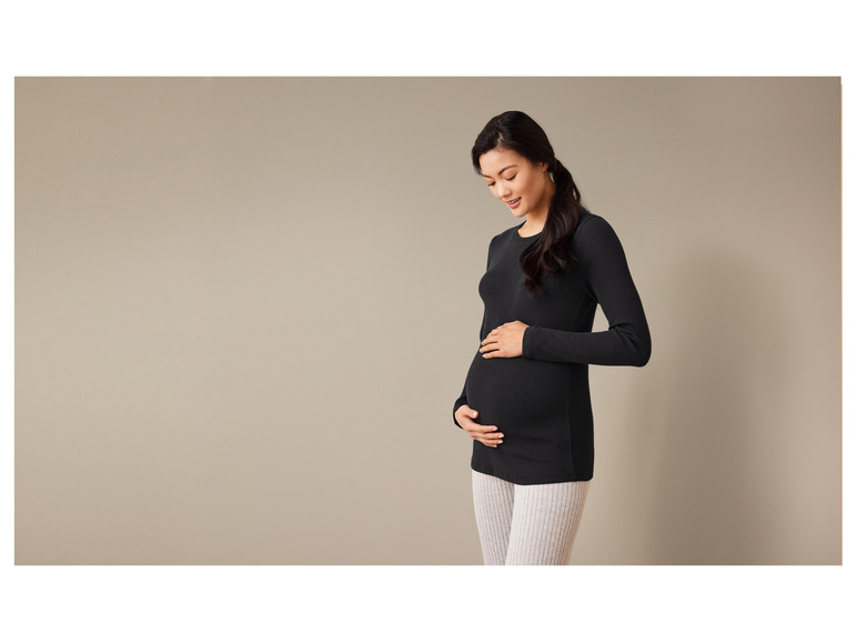 Eine schwangere Frau in einem schwarzen Oberteil und grauen Leggings.