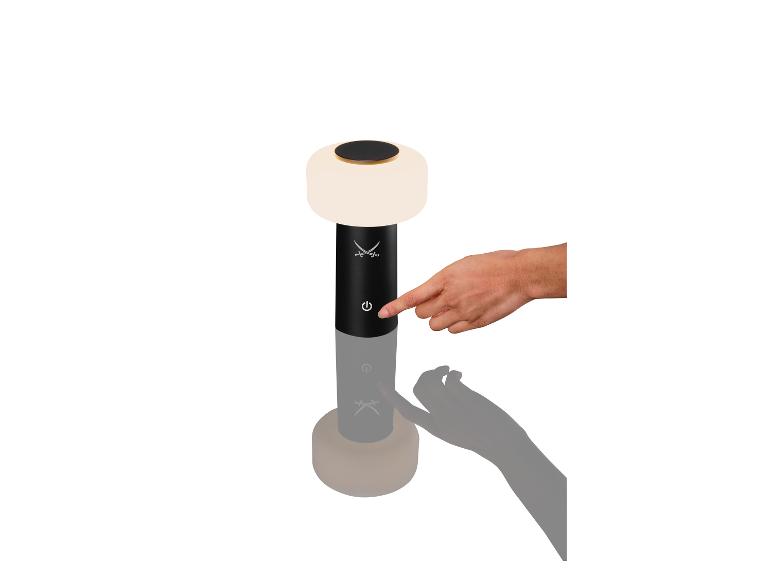 Eine Hand drückt den Einschaltknopf einer schwarz-weißen Tischlampe.