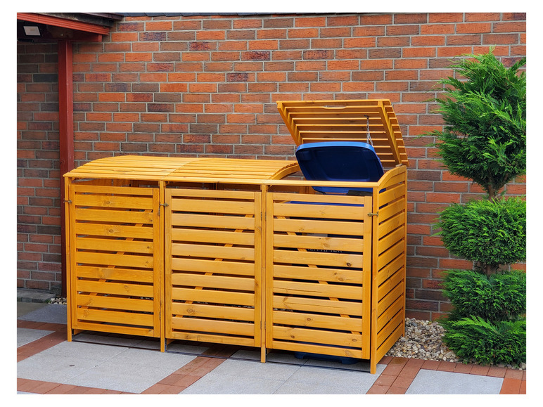 Ein dreiteiliger Holz-Abfalleimer vor einer Backsteinmauer.