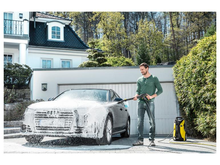 Mann reinigt Auto mit Hochdruckreiniger vor einem Haus.