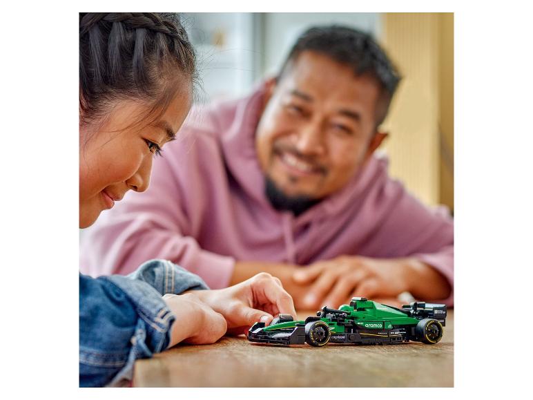 Ein Mädchen und ein Mann spielen mit einem grünen Aston Martin Aramco Rennwagen.