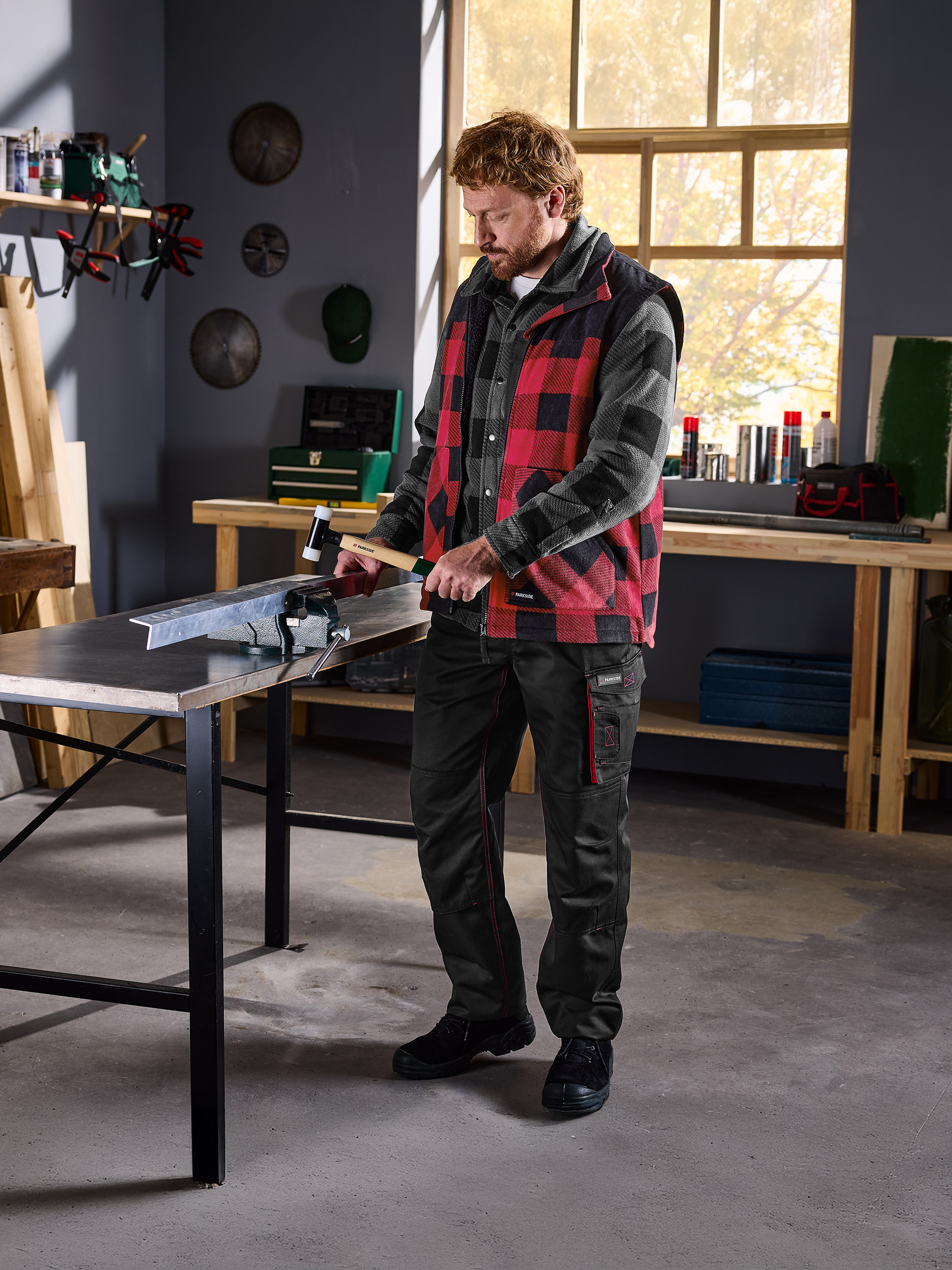 Mann in kariertem Hemd und Parkside-Weste bearbeitet Metall in einem Schraubstock in einer Werkstatt.