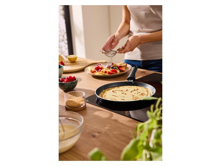 Person bereitet Crêpes mit Beeren und Zucker in einer Pfanne in der Küche zu.