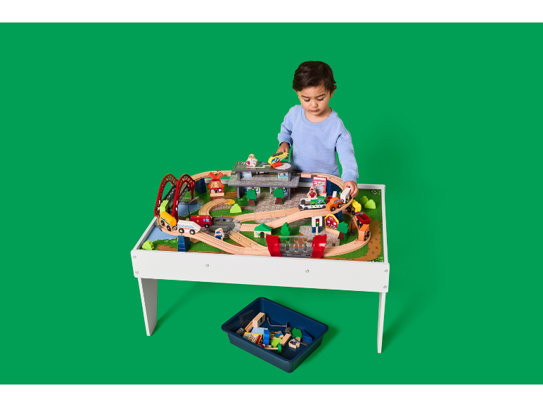 Kind spielt mit einem Holztisch mit Eisenbahn und Zubehör.