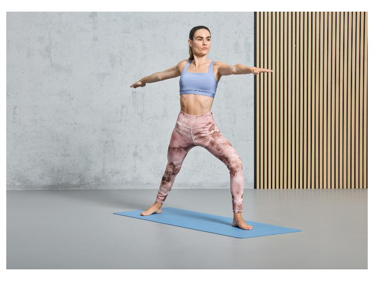 Eine Frau in Sport-BH und Leggings macht Yoga auf einer blauen Matte.