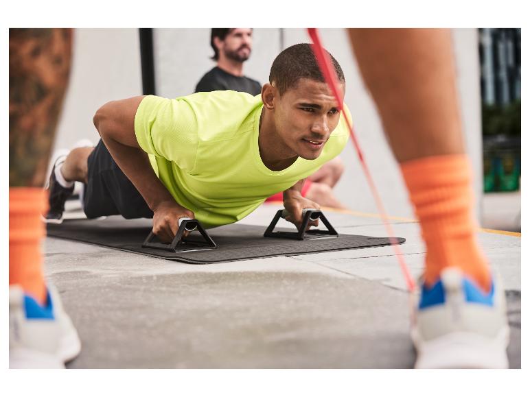 Mann macht Liegestütze mit Push-up Griffen und Fitnessmatte.