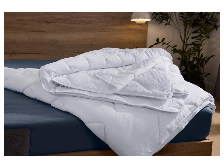 Weiße gesteppte Decke mit Muster auf einem dunkelblauen Bett im Schlafzimmer.