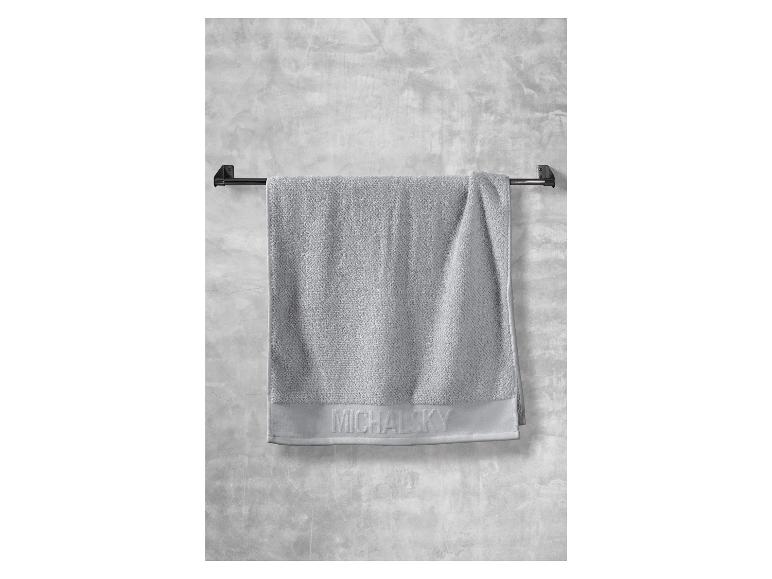 Ein graues Handtuch der Marke Michalsky hängt an einem schwarzen Handtuchhalter.