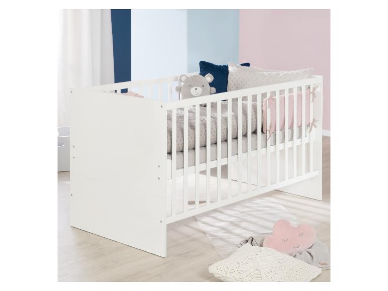 Weißes Babybett mit grauer Bettwäsche und Zierkissen, in einem Zimmer mit zweifarbigen Wänden.