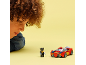 Ein Kind betrachtet eine Spielzeug-Superheldenfigur und ein rotes Spielzeugauto auf gelbem Grund.
