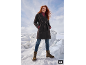 Frau in dunklem Mantel, rotem Rollkragenpullover, Jeans und braunen Stiefeln in Schneelandschaft.