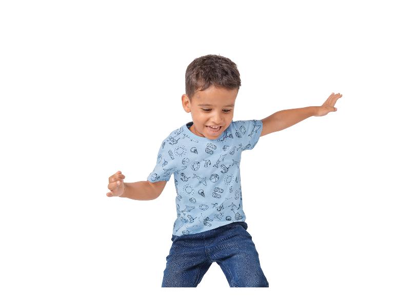 Junge springt, trägt blaues T-Shirt mit Sommermotiv und Jeans.