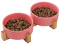 Zwei rosafarbene Näpfe mit Hundefutter auf einem Holzständer.