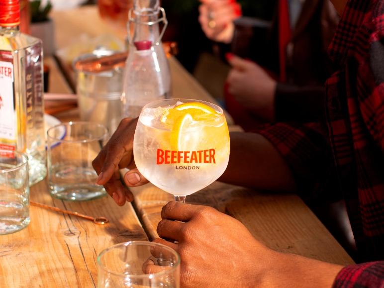 Eine Person hält ein Gin-Tonic-Glas, garniert mit Orangenscheiben, auf einem Holztisch.