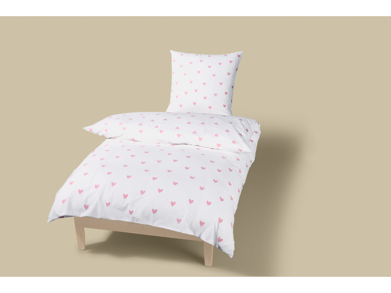 Weiße Bettwäschegarnitur mit rosa Herzmuster auf einem Holzbett.