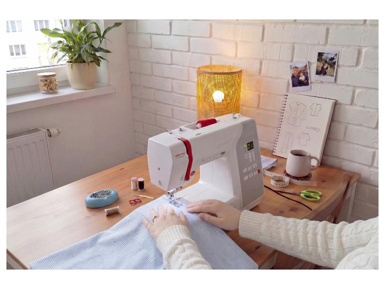 Frau näht mit Nähmaschine, Fäden, Schere und Kaffeetasse auf dem Tisch.
