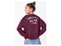 Mädchen in bordeauxrotem Sweatshirt mit „CROISSANT & COFFEE CLUB“ auf dem Rücken, Hände in den Hosentaschen.