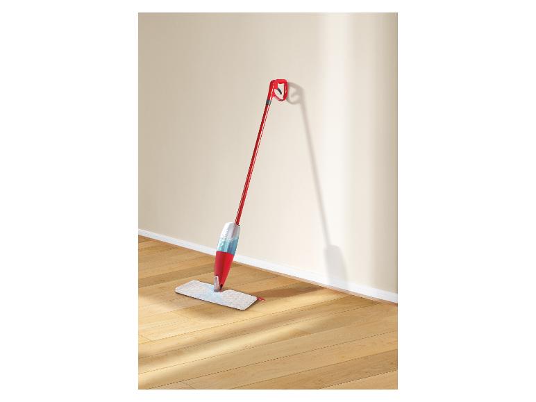 Roter und weißer Sprühmopp lehnt an einer beigen Wand mit Holzboden.