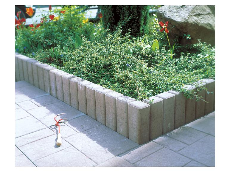 Beton-Gartenrandstein begrenzt ein Blumenbeet mit einer kleinen Harke.