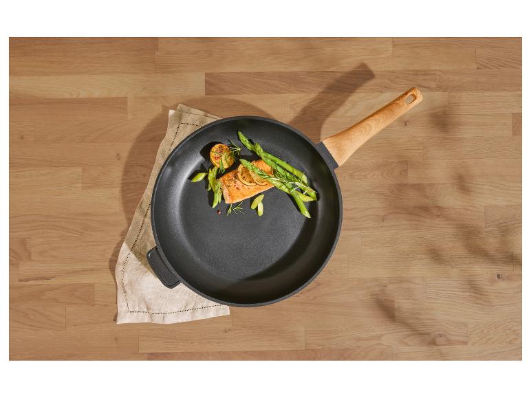 Pfanne mit Lachs, Spargel und Zitrone auf einem Holztisch.