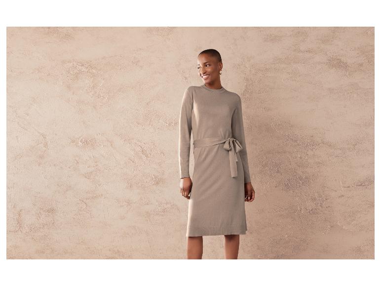 Eine Frau trägt ein beiges Strickkleid mit Gürtel.