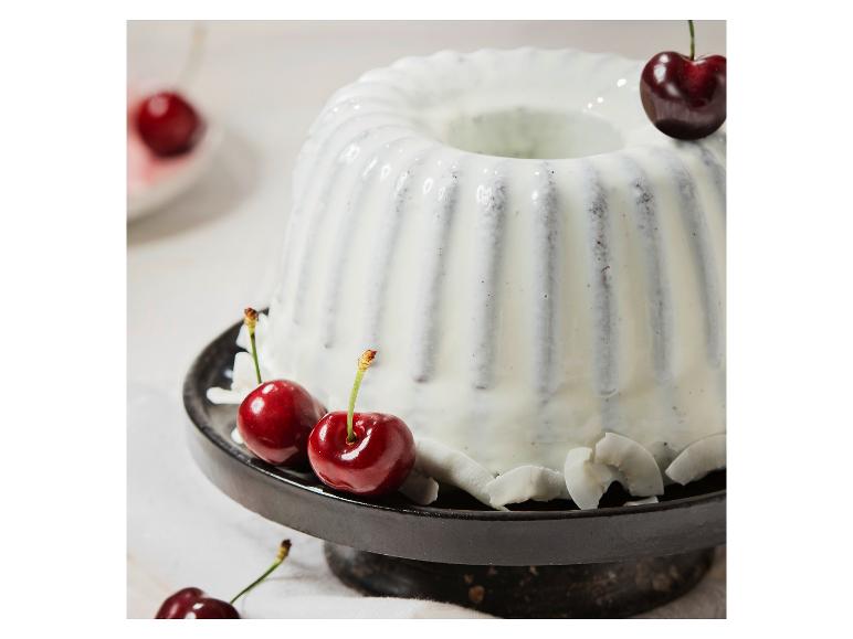 Gugelhupf mit weißer Glasur, Kirschen und Kokosflocken auf einem schwarzen Ständer.