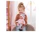 Lächelndes Mädchen hält eine Babypuppe in rosa Kleidung und Mütze.