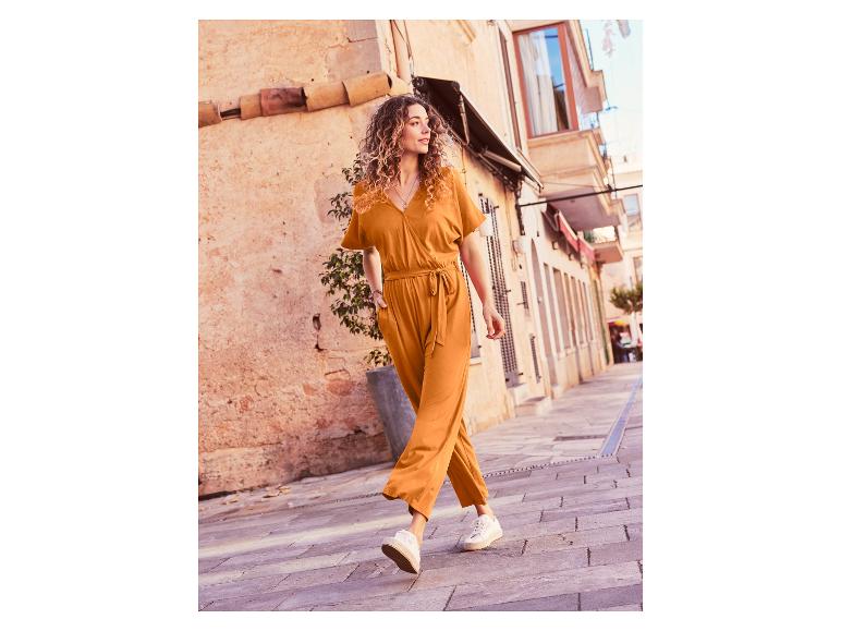 Eine Frau geht in einem orangenen Jumpsuit und weißen Sneakern durch eine Straße.