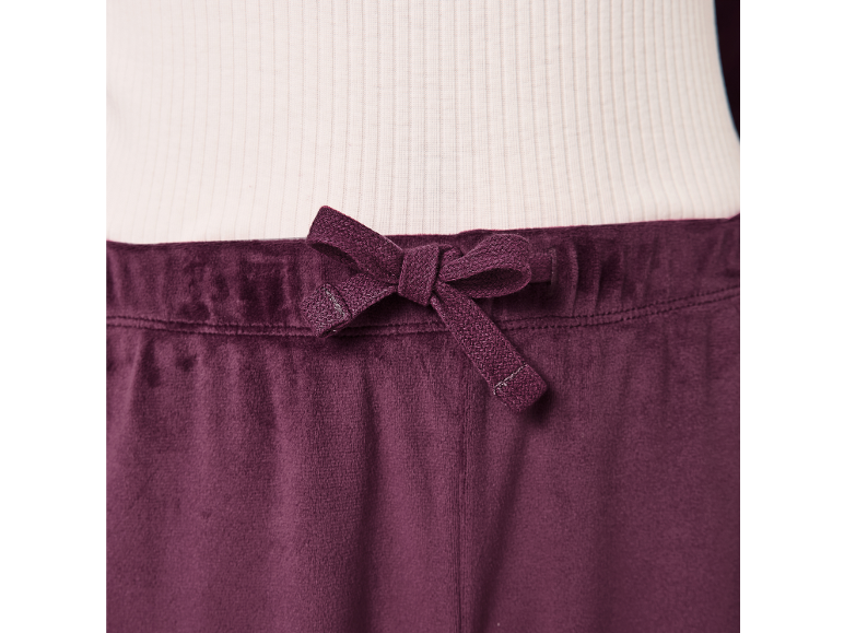 Dunkelviolette Velourhose mit Kordelzug in der Taille, kombiniert mit einem gerippten weißen Oberteil.