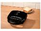 Schwarzer Sandwichmaker mit zwei Scheiben Brot auf einem Teller auf einer Holzoberfläche.
