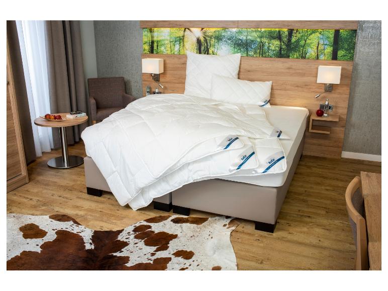 Modernes Schlafzimmer mit Bett, weißer BeCo-Bettwäsche, Nachttischen aus Holz und einem Kuhfellteppich.