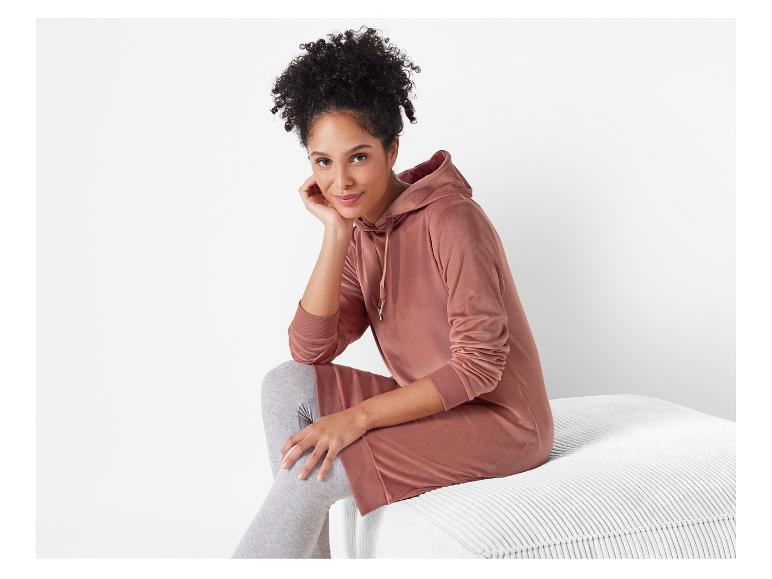 Eine Frau trägt ein rosafarbenes Hoodie-Kleid mit grauen Leggings.